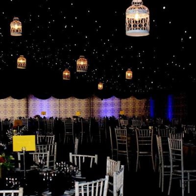 A party scene with Brunel fabric wall linings and star cloth ceiling linings with lights overhead and tables laid for dinner