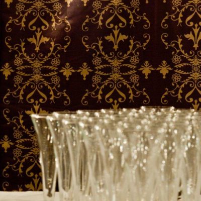 A marquee wall lining with purple and gold design behing a set of champagne flutes ready to pour