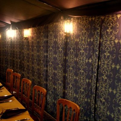 A long wall of Brunel fabric wall linings with pretty lights strung across it and dining tables in front of it