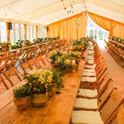 Saffron marquee wall linings with bespoke reveal curtain for a wedding marquee and wooden tables and chairs set out