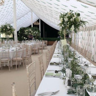 A marquee wall lining with a fern leaf printed design repeated overhead and on the walls and tables laid for a meal