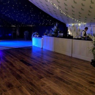 A marquee dancefloor with bespoke printed linings overhead a long bar and soft blue lighting