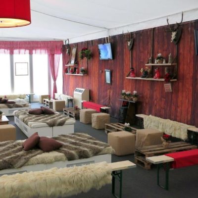 A seating area with rustic furniture, furs, props and Apres Ski themed marquee linings in red and white gingham and wood plank walls