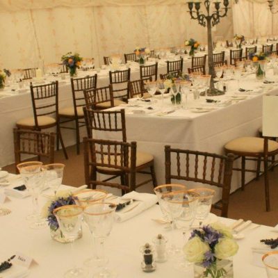 A dining room in a marquee with tables and chairs laid up and Jasmine wall linings behind it