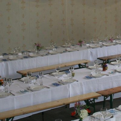 Long tables and benches set up for a wedding breakfast in a barn transformed with Jasmine wall linings