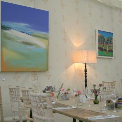 Paintings hang on a marquee wall with Jasmine wall linings and tables set for dining