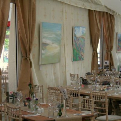 Hessian curtains frame the windows inside a marquee set for dining with paintings on the wall