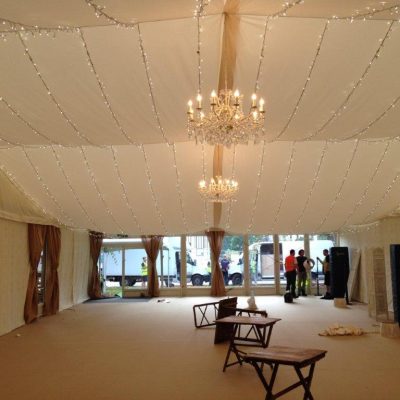A marquee has plain white ceilings chandeliers and fairy lights with Jasmine wall linings