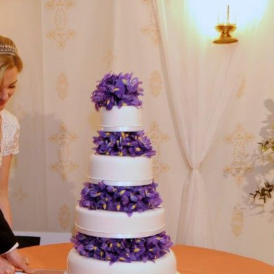 A four tier wedding cake in a marquee with the bride and goorm cutting the cake against a Jasmine wall lining