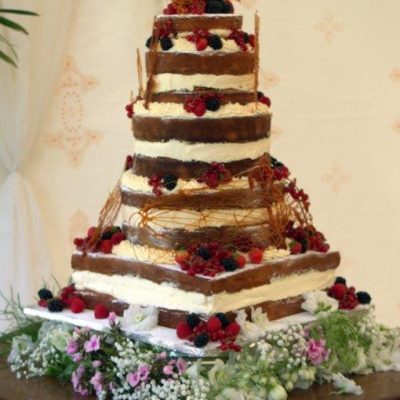 A layered cake stands on a table with a Jasmine wall lining backdrop