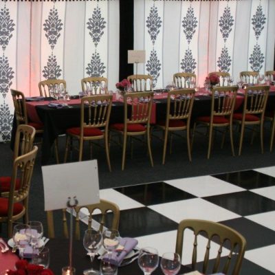 A marquee party with black white and grey linings and pink table cloths next to a chequered dance floor
