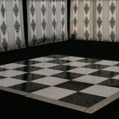 A marque with black white and grey marquee linings black carpet and an angled chequerboard black and white dance floor on black carpet