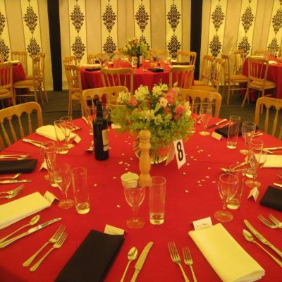 A round dining table with a ruby red table cloth in a maquee with a Rococo backdrop
