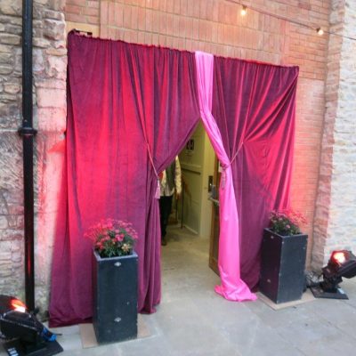 Velvet drapes are decorated with a pink fabric twist in the spotlight of a party entrance