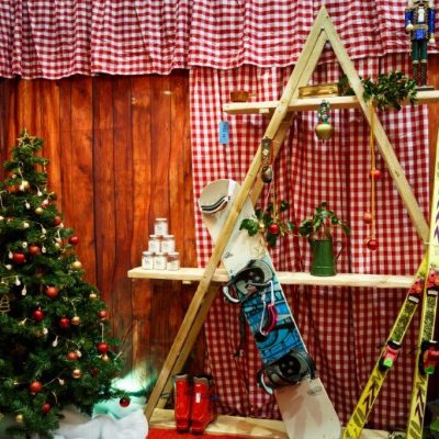 A triangular shaped prop shelf featuring Christmas style items inside a marquee dressed with gingham and wood plank effect wall linings