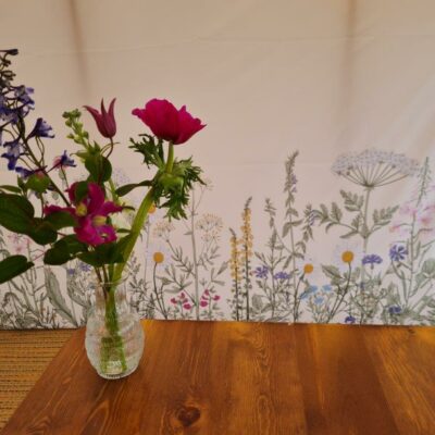 Botanical marquee wall linings hang behind a wooden table with a simple Spring flower vase